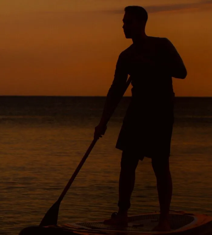 Silhouette of a man paddleboarding during sunset, reflecting chilling stories of gut feeling.