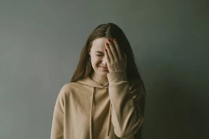 A young woman doing a facepalm after one of many funny instances of everyday failure.