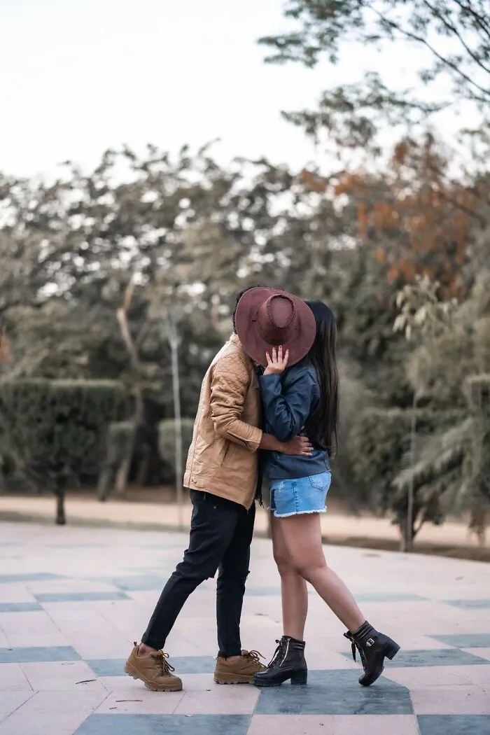 A young couple sharing a kiss in a park, connecting to school rumors about secret student relationships