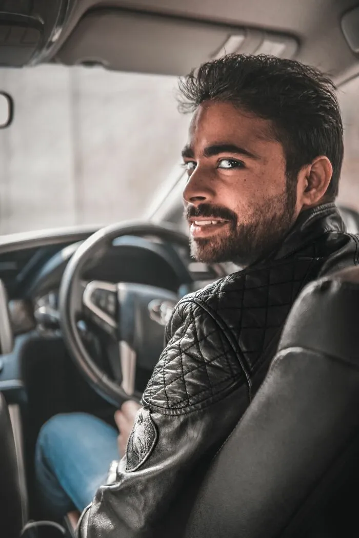 A smiling driver looking back from the front seat of a car, ready to leave immediately