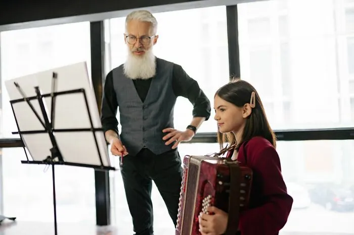 Elderly music teacher watching a young girl play accordion, confirming school rumors about talented staff.