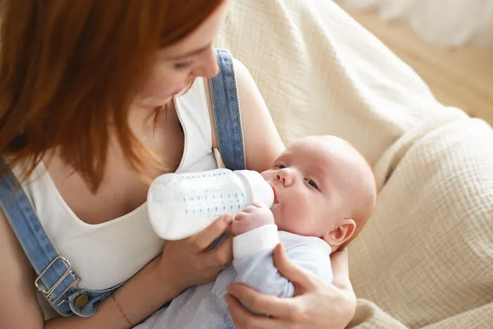 A mother bottle-feeding her baby while holding him closely.