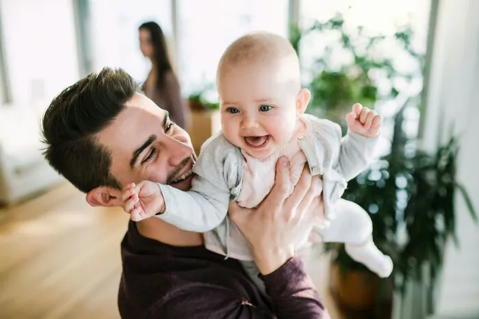 A smiling father holding his joyful baby up in the air, embodying positive masculinity and compassionate parenting.