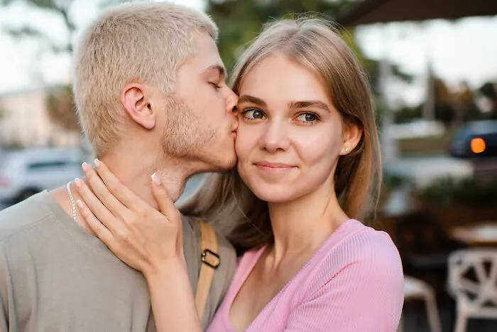 Blonde man kissing his partner on the cheek as an example of positive masculinity and affection.