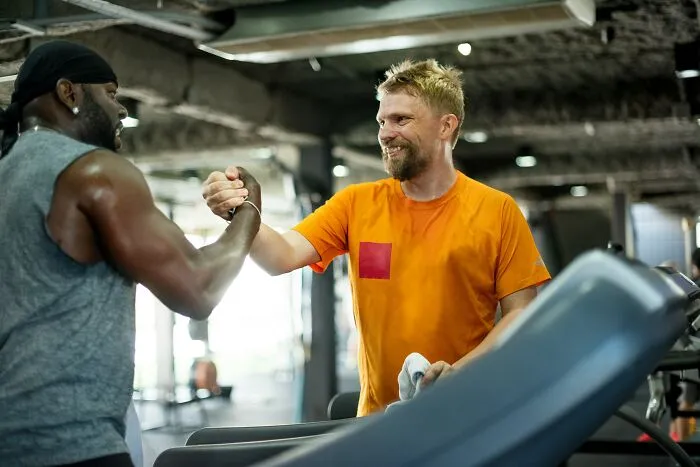 Two supportive male friends shaking hands and smiling at the gym, representing positive masculinity and camaraderie.
