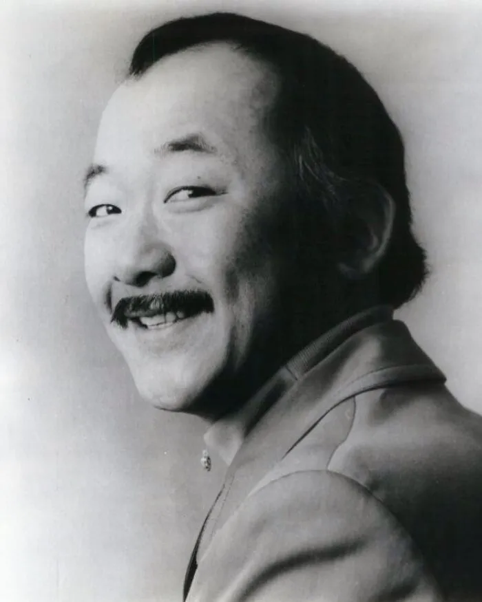 A black-and-white portrait of a smiling man with a mustache, demonstrating positive masculinity and warmth.