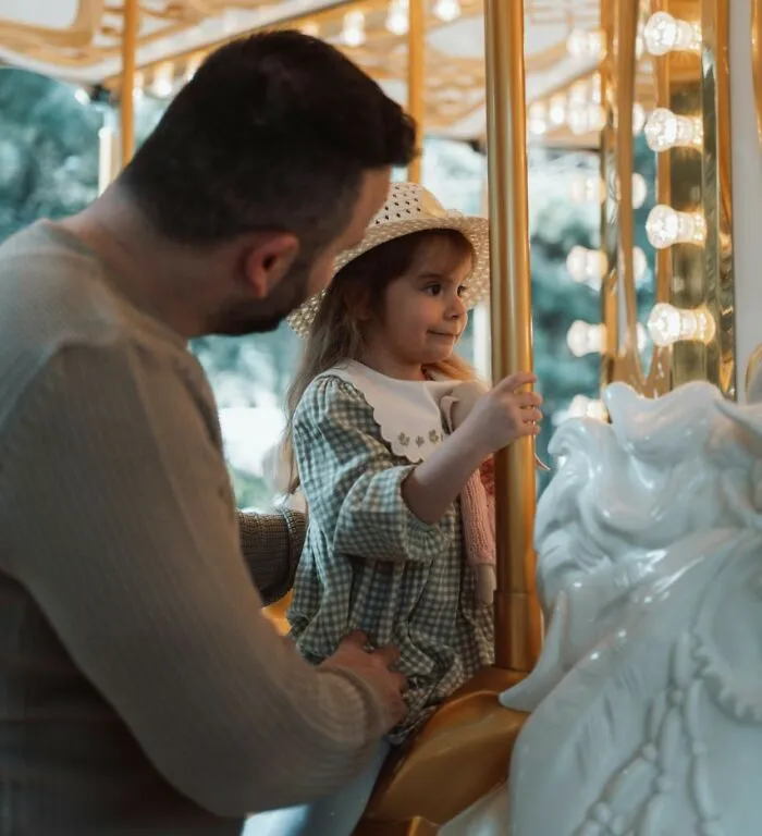 A caring father helping his young daughter on a carousel, showing positive masculinity in parenthood