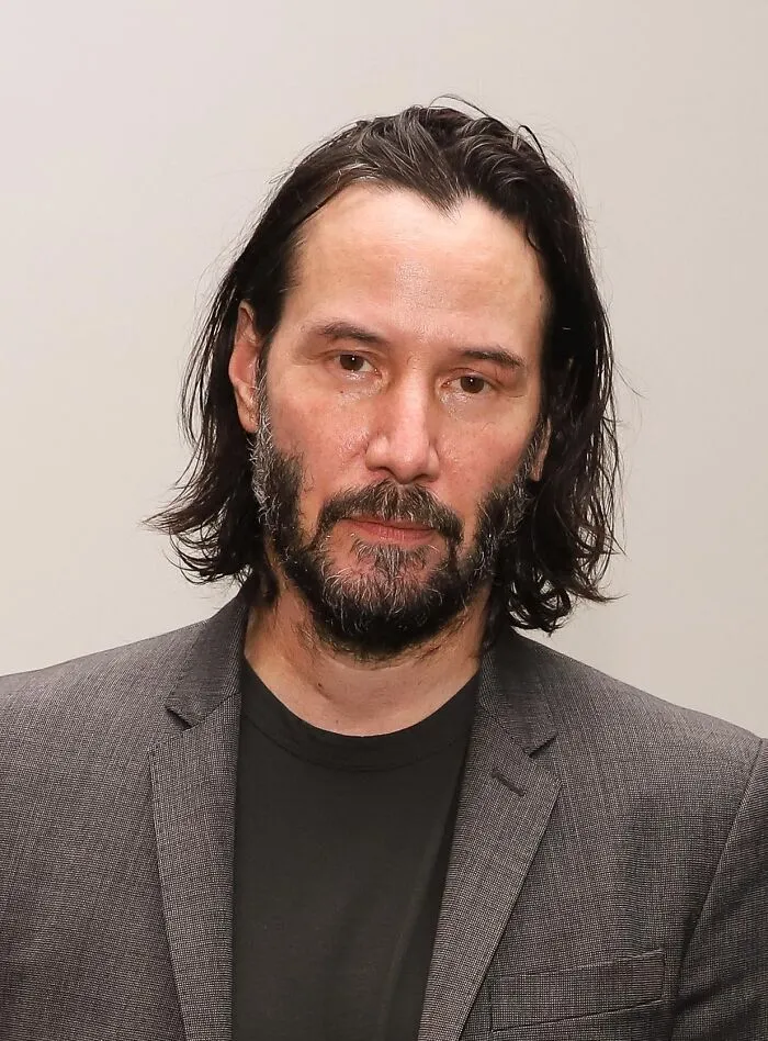 Portrait of Keanu Reeves in a gray suit, well known for embodying positive masculinity and kindness