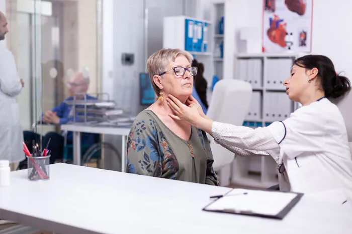 A female doctor examining a senior patient neck during a medical consultation.
