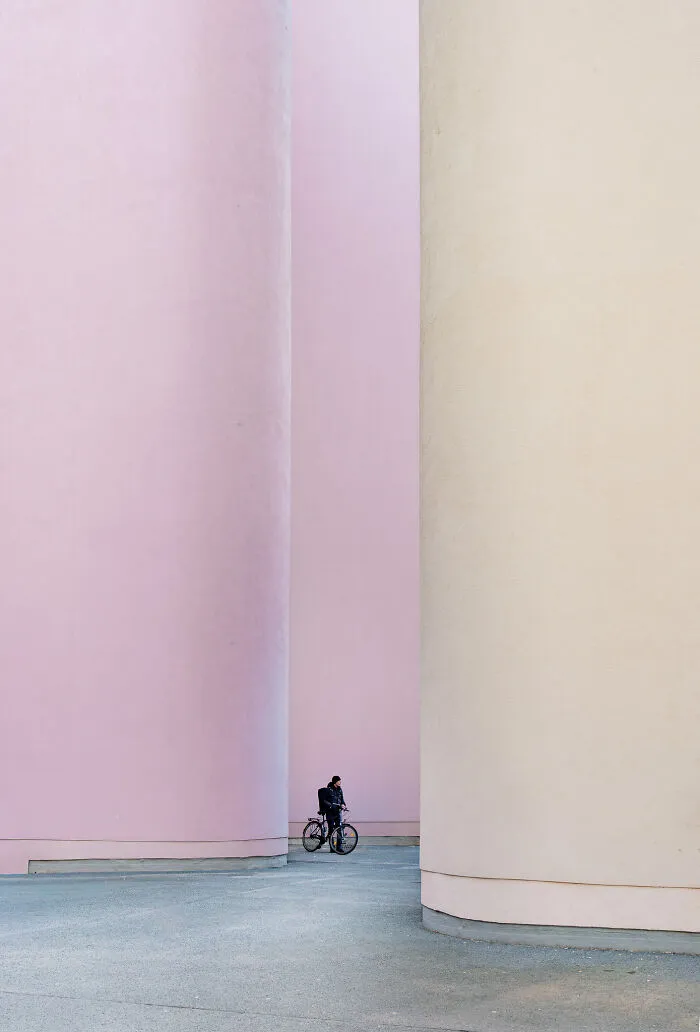A cyclist riding between massive pink and beige curved structures, displaying the beauty of spaces