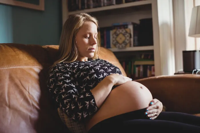 Pregnant young woman sitting on a sofa, highlighting rising Gen Z health problems.