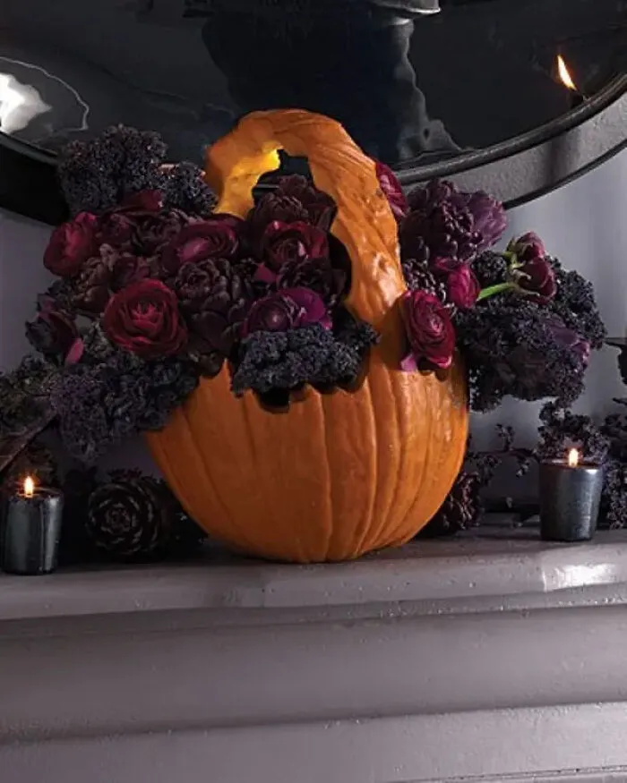 A carved pumpkin flower basket filled with dark purple flowers and kale for spooky Halloween homes.