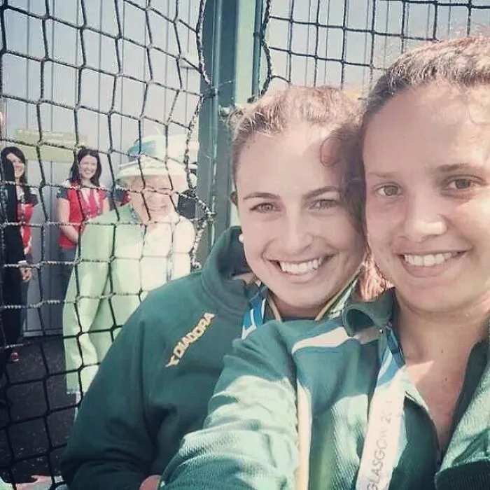 Queen Elizabeth photobombs two smiling women in the background of a selfie through a fence