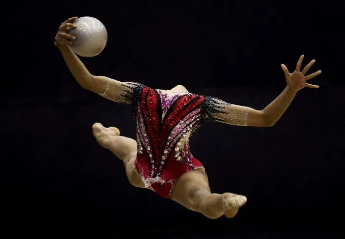 Rhythmic gymnast in mid-air performing with ball in dramatic light, best pics 2026 Siena International Photo Awards