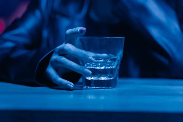 Hand holding a glass of liquid under blue light, illustrating someone who got fired early on