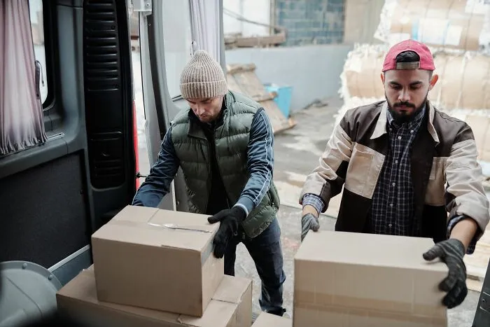 Two delivery workers loading cardboard boxes into a van, representing people who got fired early on.
