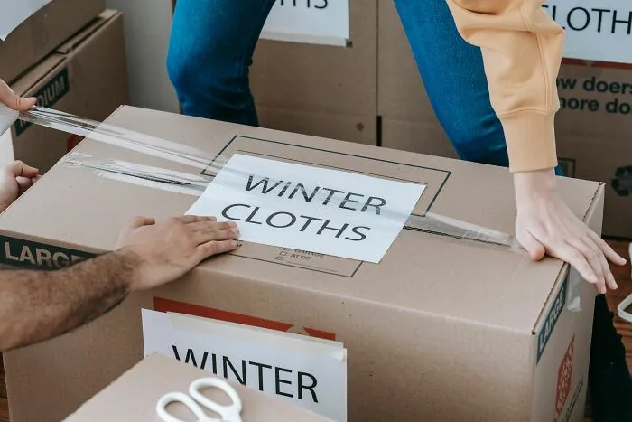 Volunteers taping up a cardboard box labeled winter clothes for donation.
