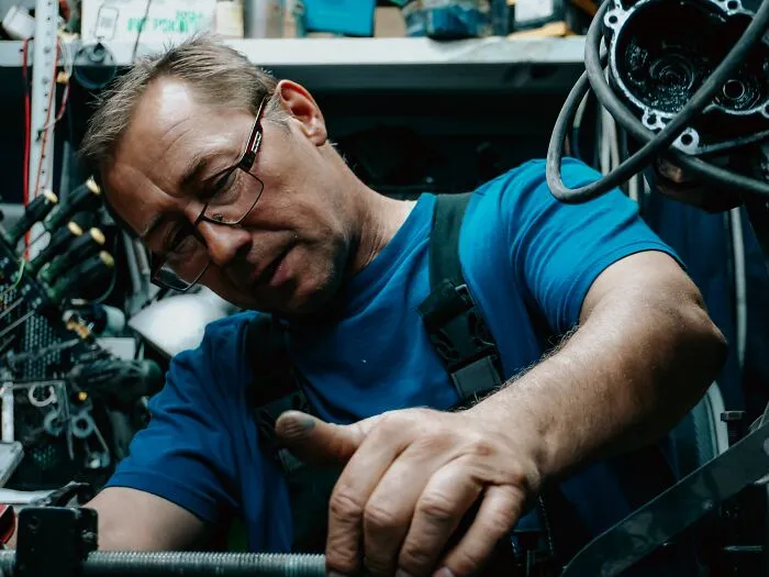 A focused mechanic in glasses working diligently in a workshop before getting fired