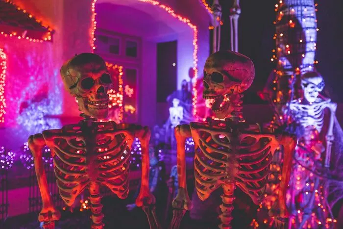 Spooky Halloween skeleton decorations illuminated in glowing pink light outside a house