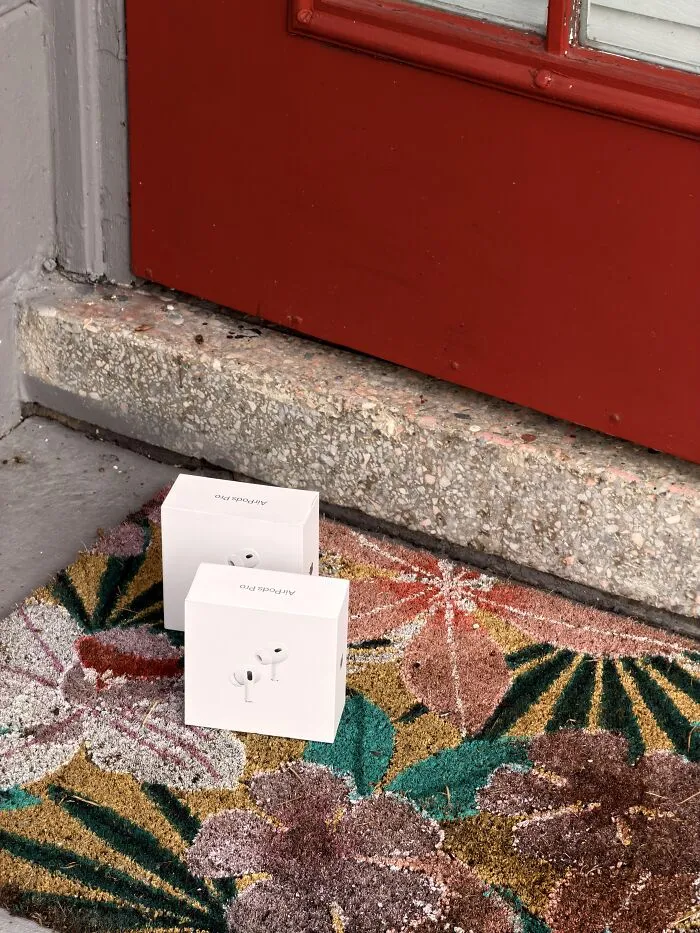 Two small package boxes sitting on a colorful doormat outside a red door.