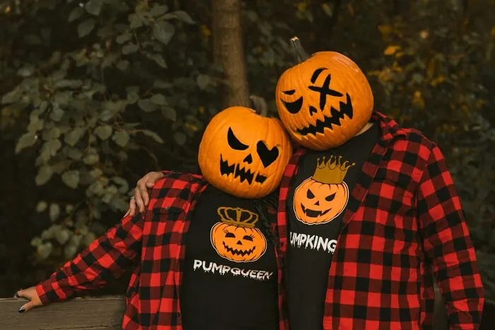 A couple posing in matching red plaid shirts and scary pumpkin heads for Halloween