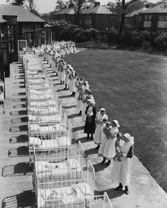 Nurses lined up with babies in cribs outside a historical orphanage