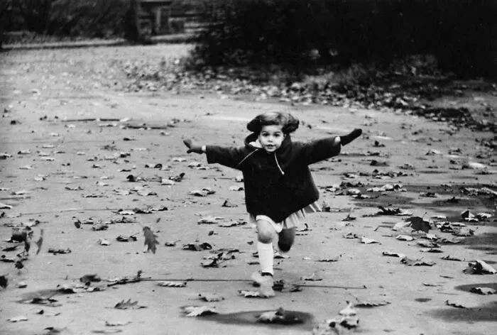 Black and white rare historical photo of a child running on a leaf-strewn path
