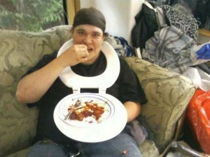 A man sitting on a couch eating food off a plate held inside a toilet seat, showcasing genius redneck fixes.
