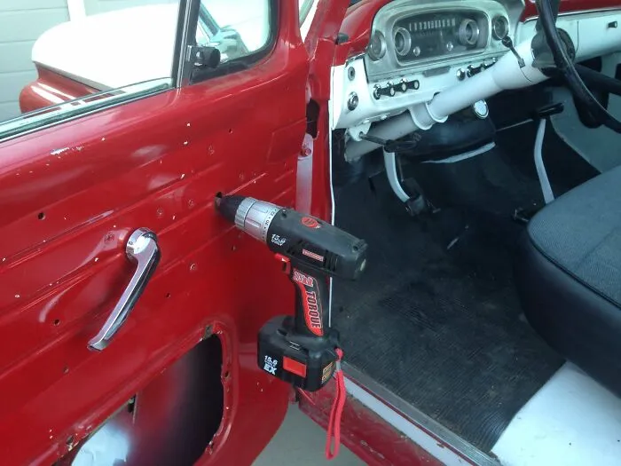 A power drill attached to a vintage car door mechanism to act as a window crank, showing handy redneck fixes.