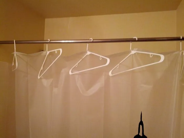 Plastic coat hangers supporting a shower curtain rod, showcasing creative redneck fixes.