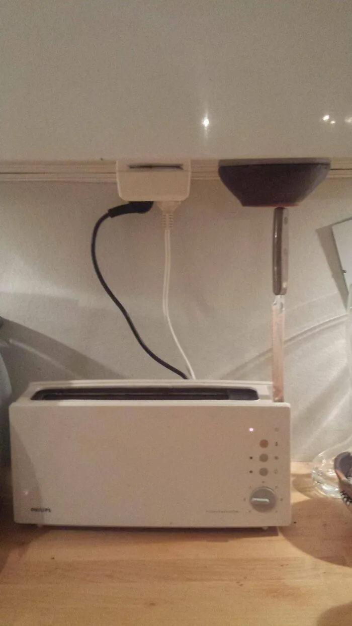 An unconventional redneck fix using a knife under a kitchen cabinet to hold down a toaster lever.