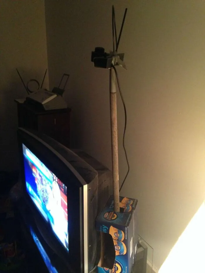 A makeshift TV antenna fixed using a wooden stick and a macaroni box, showing creative redneck fixes.