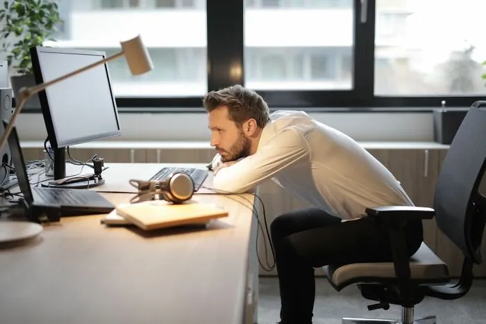 Frustrated employee leaning on a desk watching a computer screen after receiving bad bonuses from bosses