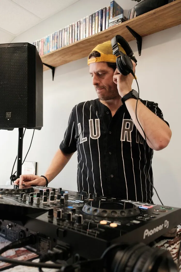 A DJ wearing a cap mixing music on a turntable console, reflecting out of touch bosses and management.