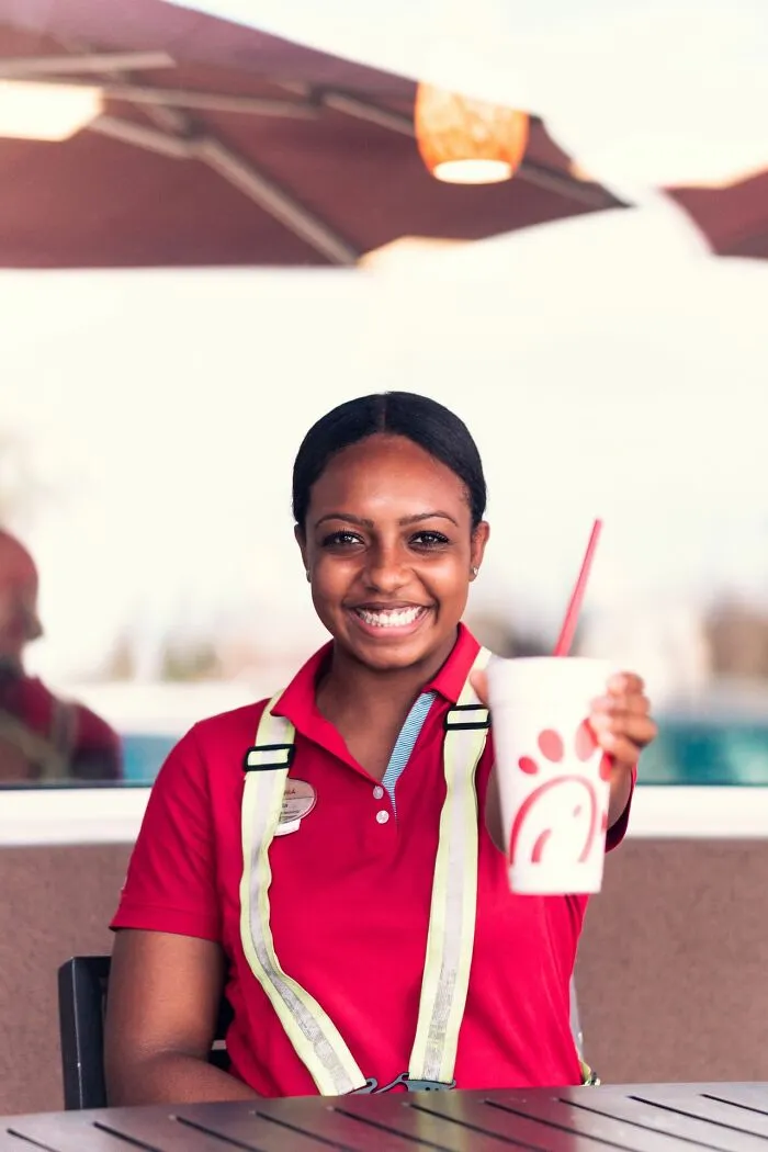 Smiling fast food worker handing over a drink, highlighting poor employee bonuses from management