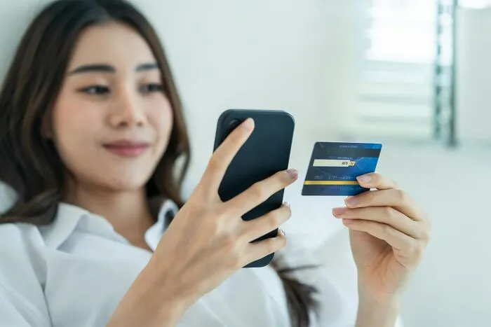 A woman holding a credit card and smartphone, symbolizing out of touch bosses and management bonuses.