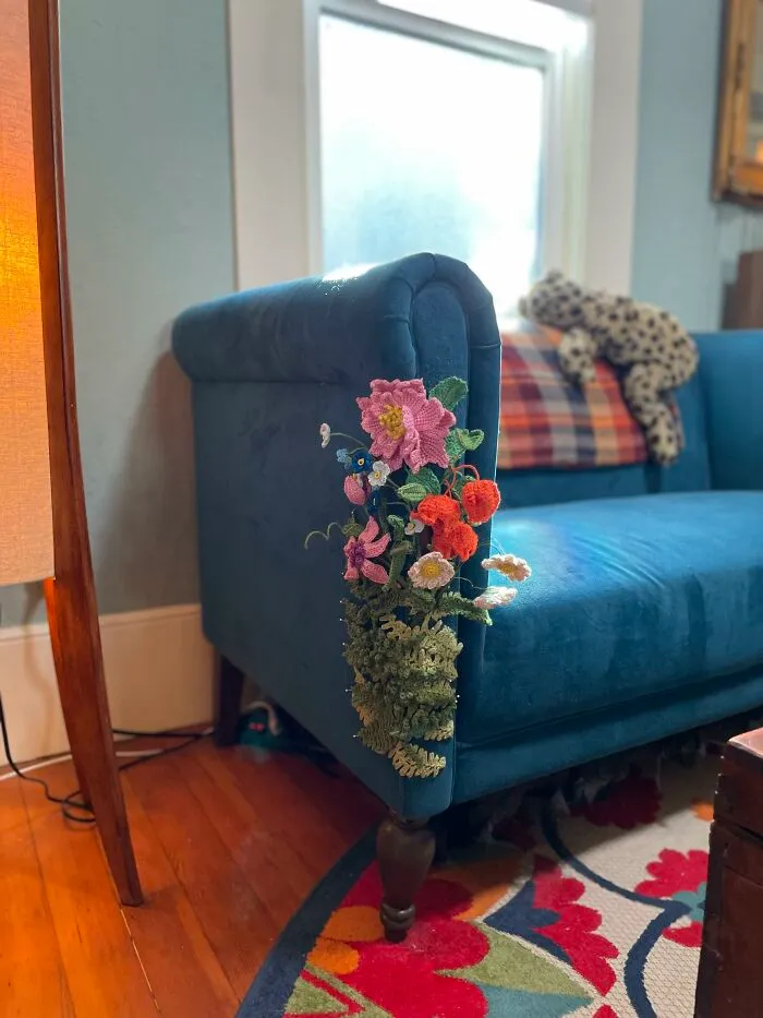 A blue velvet couch decorated with crocheted flowers on the armrest displaying creativity.