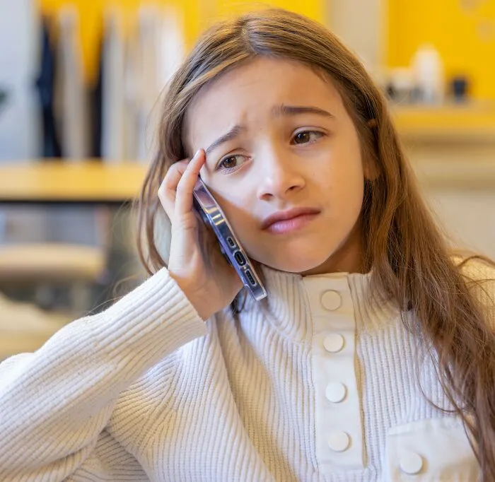 A young girl looking worried while on a phone call, representing helicopter parenting anxiety