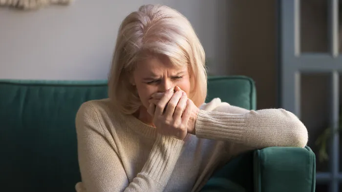 An older woman crying on a green sofa, illustrating the emotional pain of being disowned by family.
