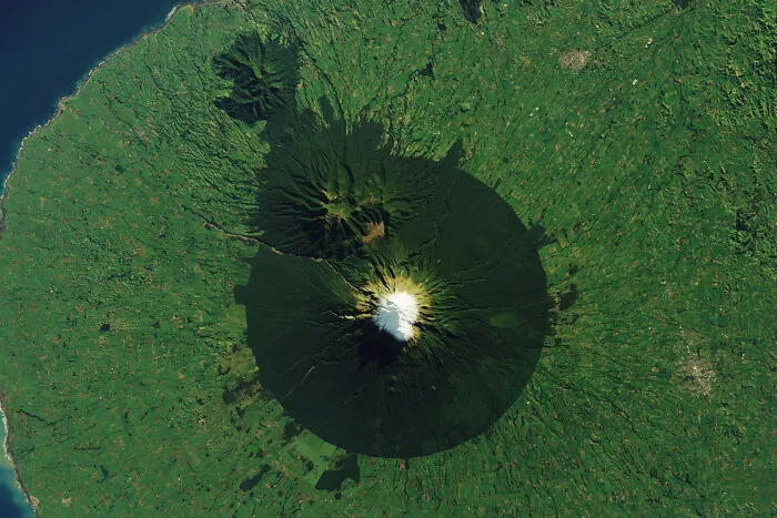 Surreal satellite photos capturing a circular green forest around a snow-capped volcano