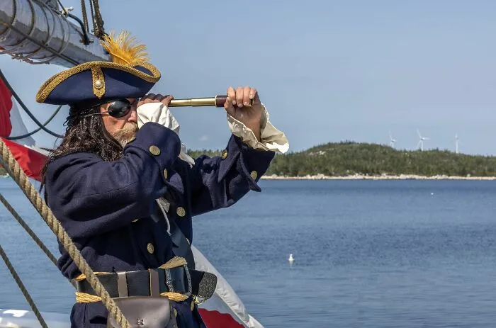 Man dressed as pirate looking through a spyglass on ship