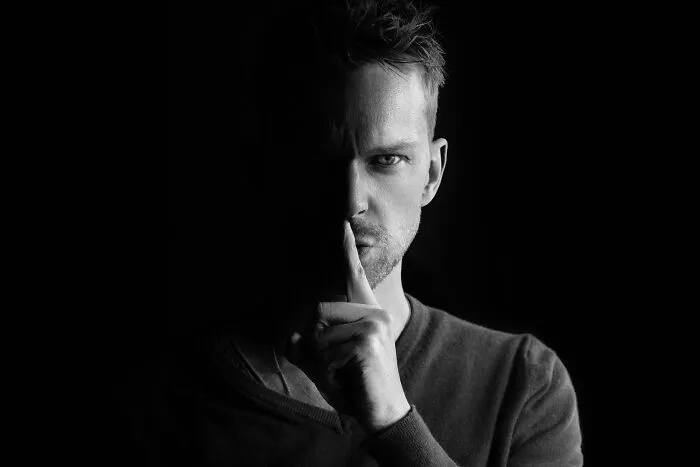 Man in low light with finger on lips for secret gesture