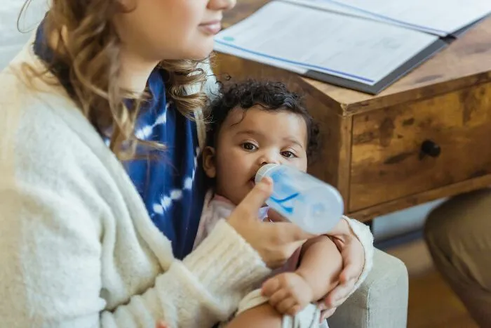 Woman feeding baby with bottle indoors, close-up of feeding moment and care