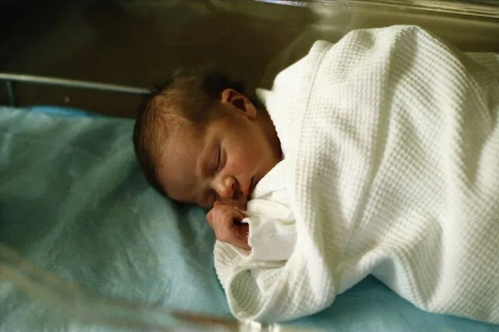 Newborn baby sleeping wrapped in white blanket in hospital crib