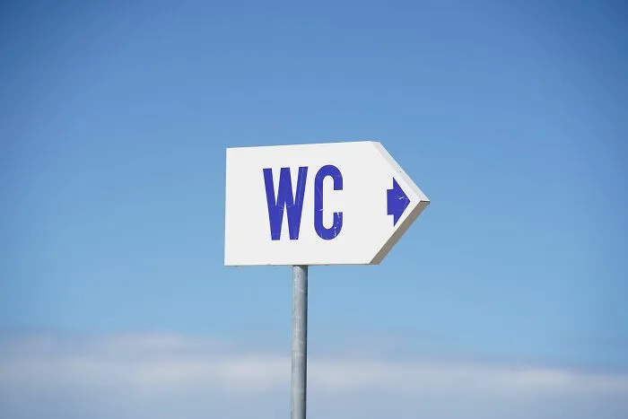 White WC sign with blue letters pointing to restroom on clear sky