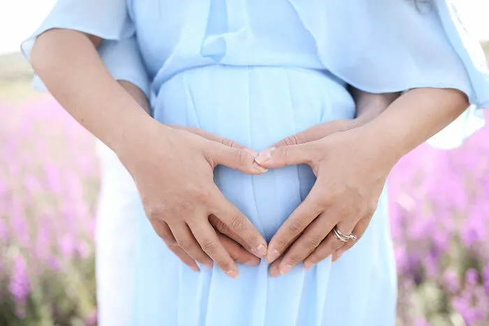 Hands forming heart shape on pregnant belly in blue dress
