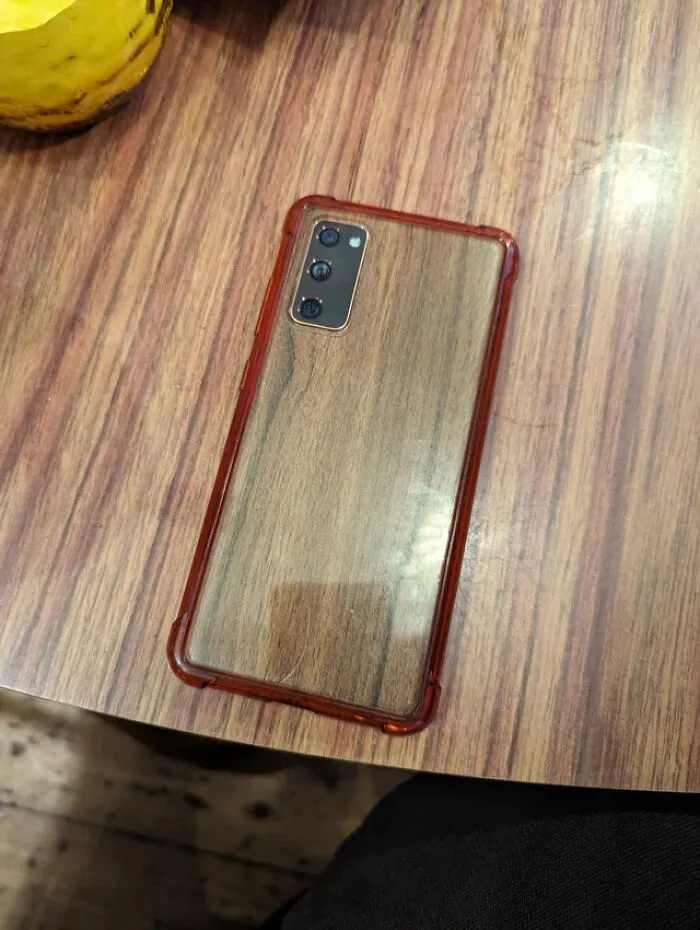 A smartphone with a clear case lying on a wooden surface blending into the wood grain creating confusing photos.