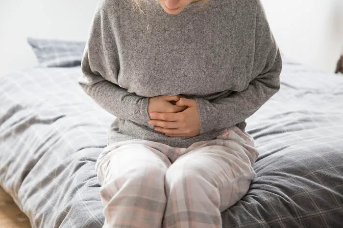 A person sitting on a bed holding their painful stomach, dealing with being sick.