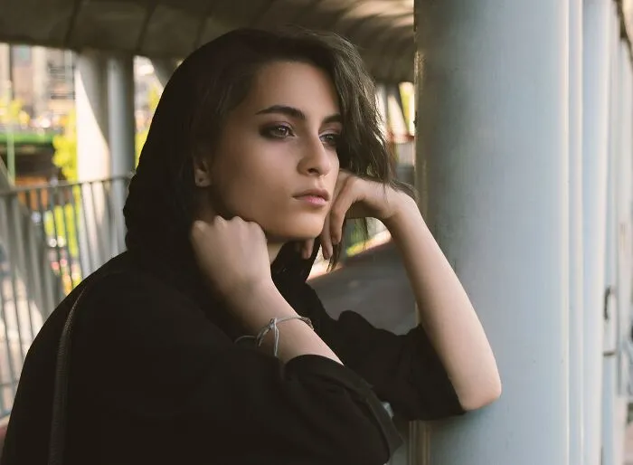 A pensive young woman leaning against a pillar outdoors, reflecting on hurt caused by narcissistic parents