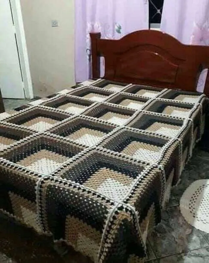 Crocheted blanket on a bed featuring a perfectly confusing optical illusion pattern of nested squares.